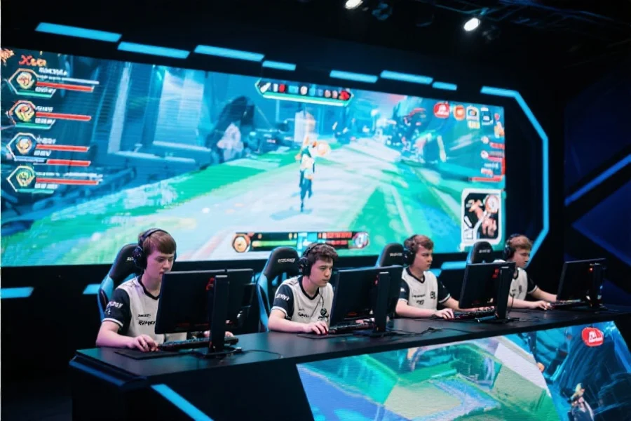 五位电竞选手坐在电脑前专注比赛，背景为大型LED屏幕显示游戏画面